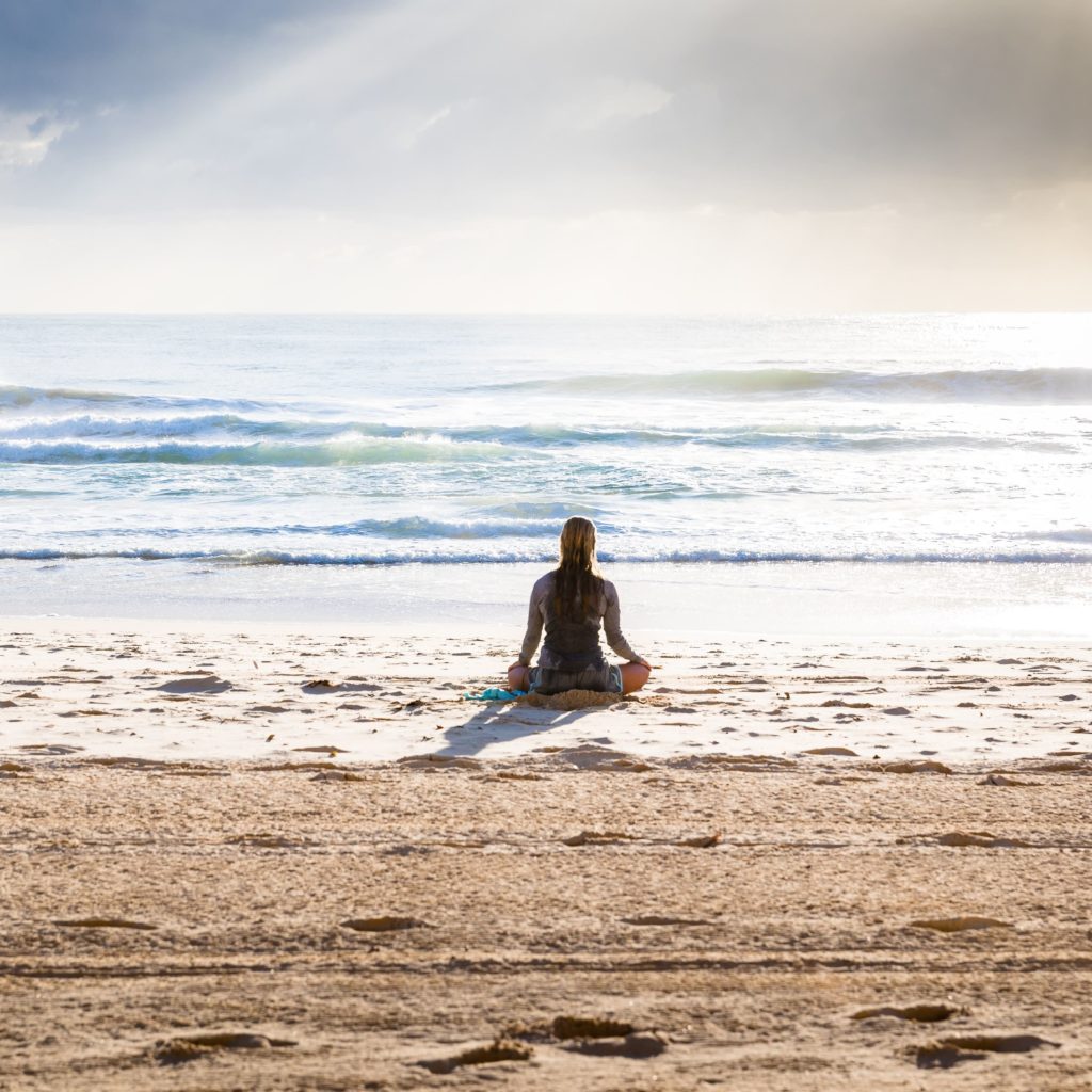 junge Frau sitzt im Schneidersitz am Strand un meditiert