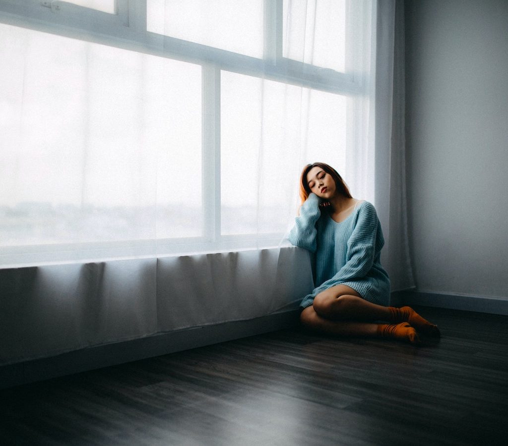 junge Frau sitzt alleine und traurig auf dem Boden und verspürt innere Leere