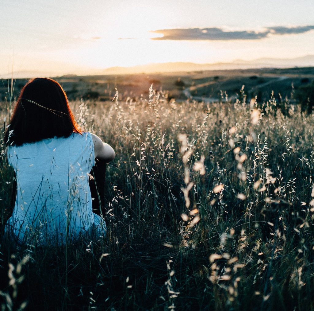 junge Frau sitzt einsam im Feld und schaut in die Ferne - Einsamkeit