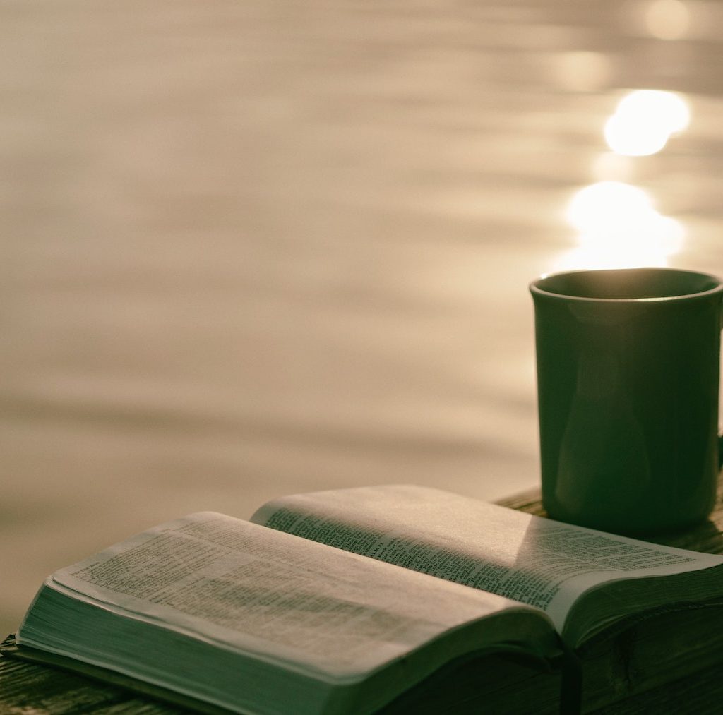Tasse heißen Kaffee neben einem Buch am Morgen - Morgenroutine hilft beim Faulheit überwinden