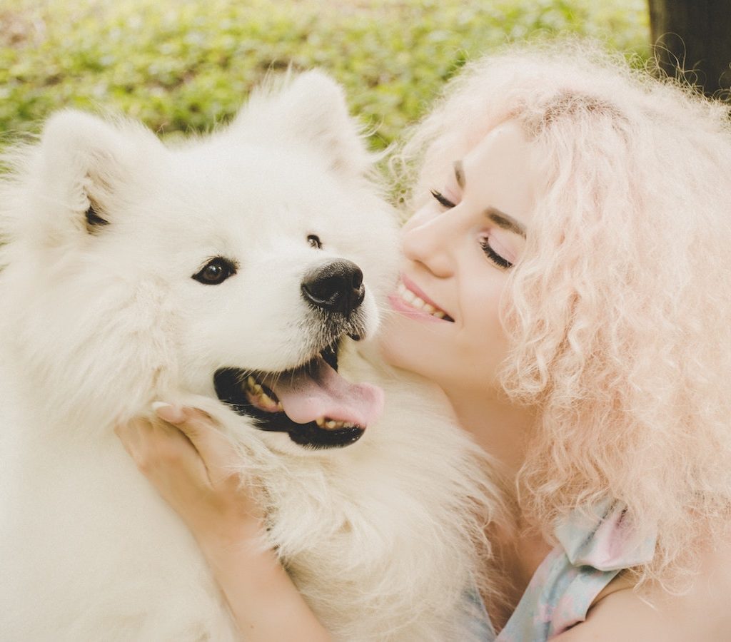 junge blonde Frau spielt mit einem weißen Hund ist fröhlich