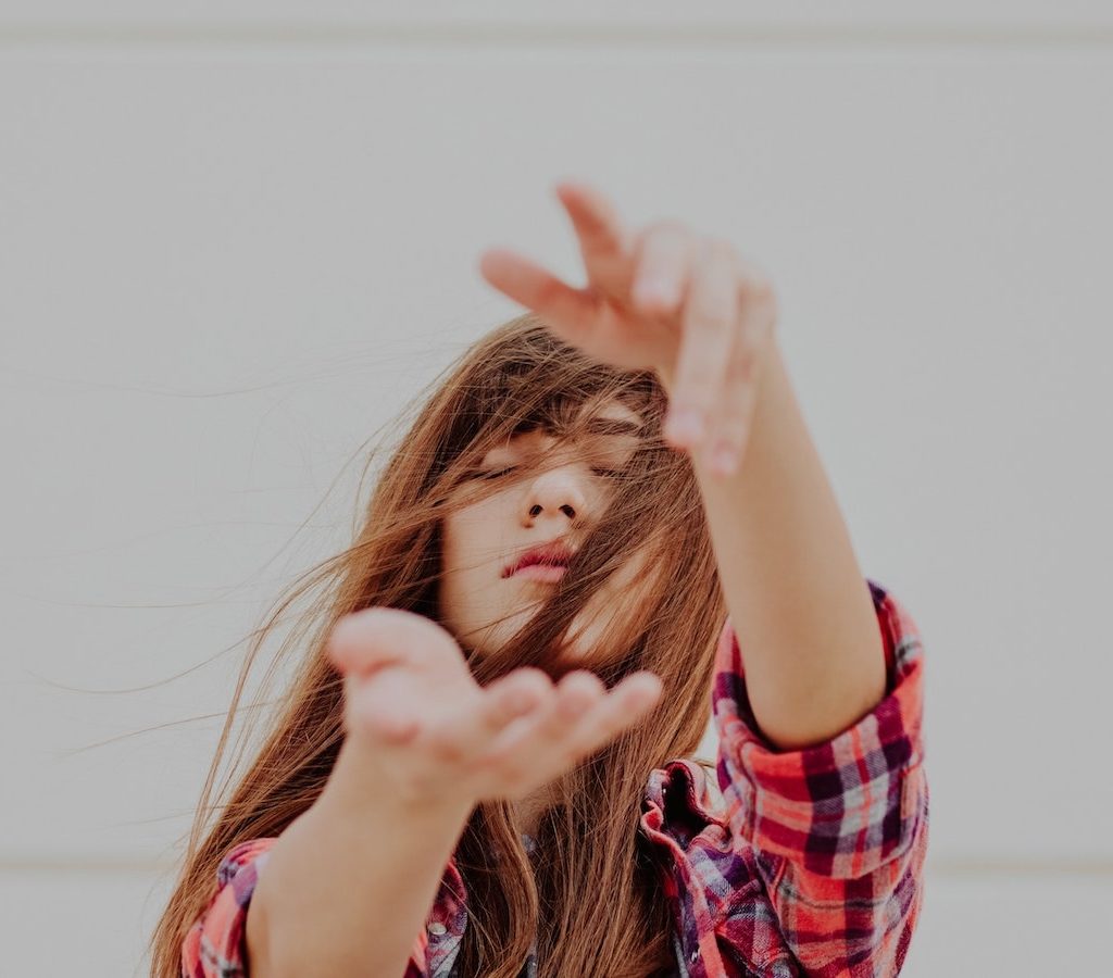 junge Frau mit geschlossenen Augen hebt ihre Hände vor sich