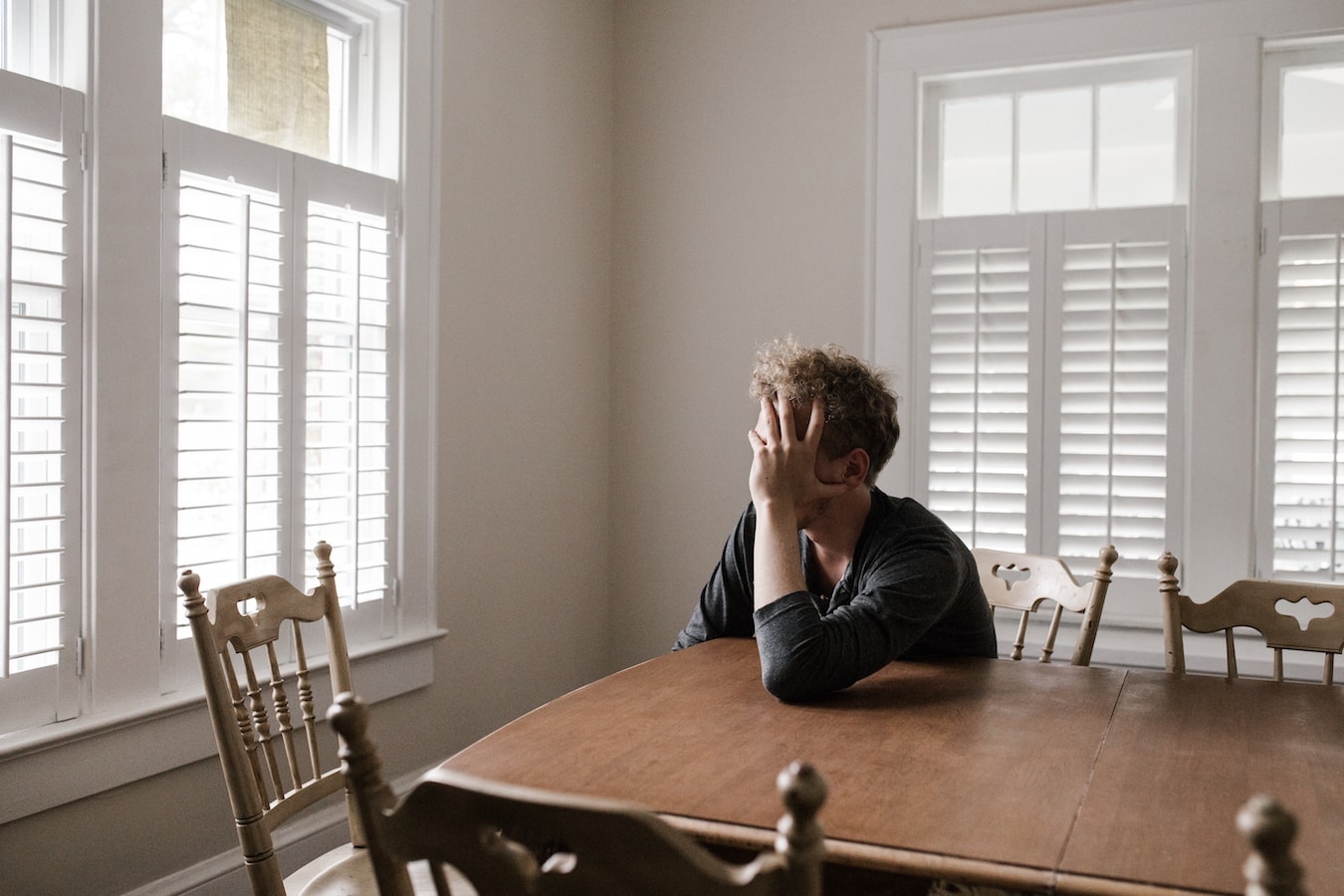 Junger Mann sitzt nachdenklich am Tisch Selbstsabotage Angstzustände Stress