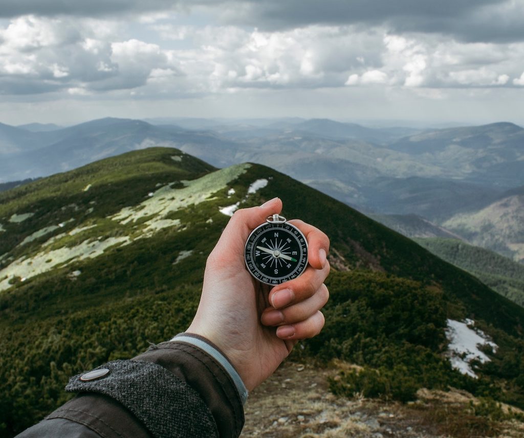 eine Hand hält einen Kompass vor einer Berglandschaft, Orientierung Ziele setzen Vision