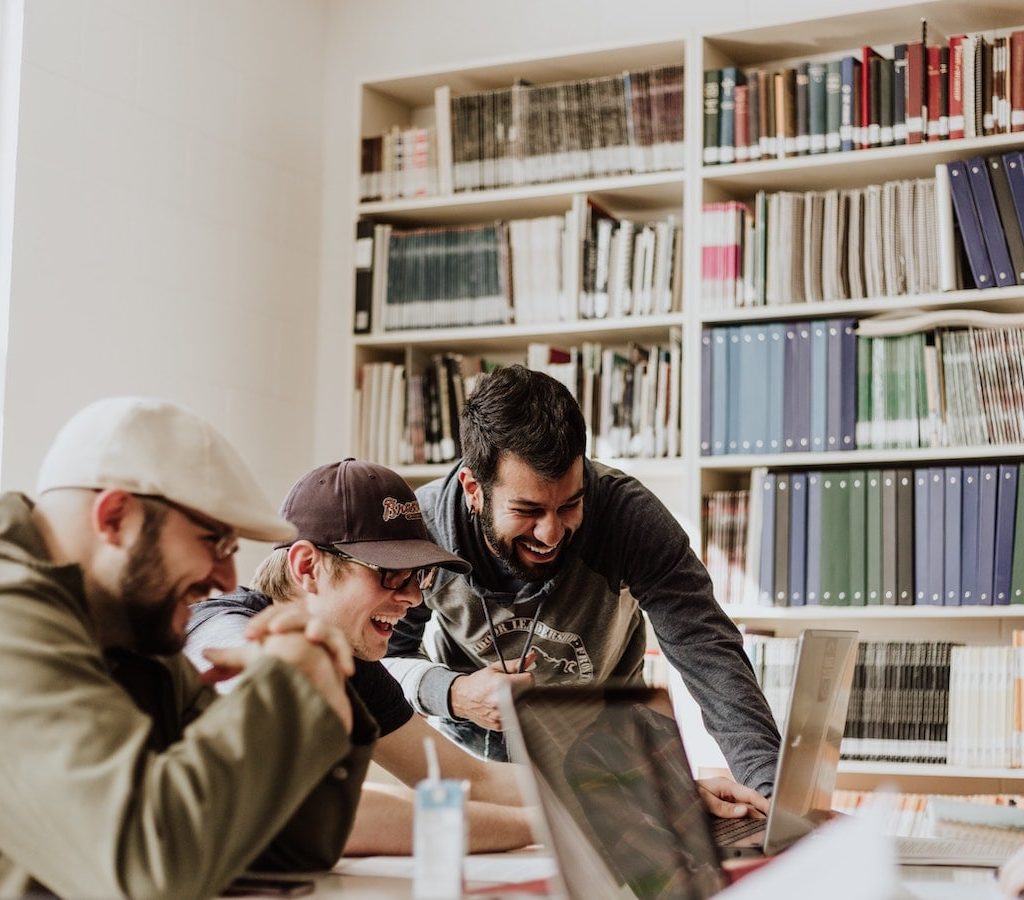 junge Männer in der Bibliothek arbeiten gemeinsam an ihren Computern und lachen - Einsamkeit überwinden