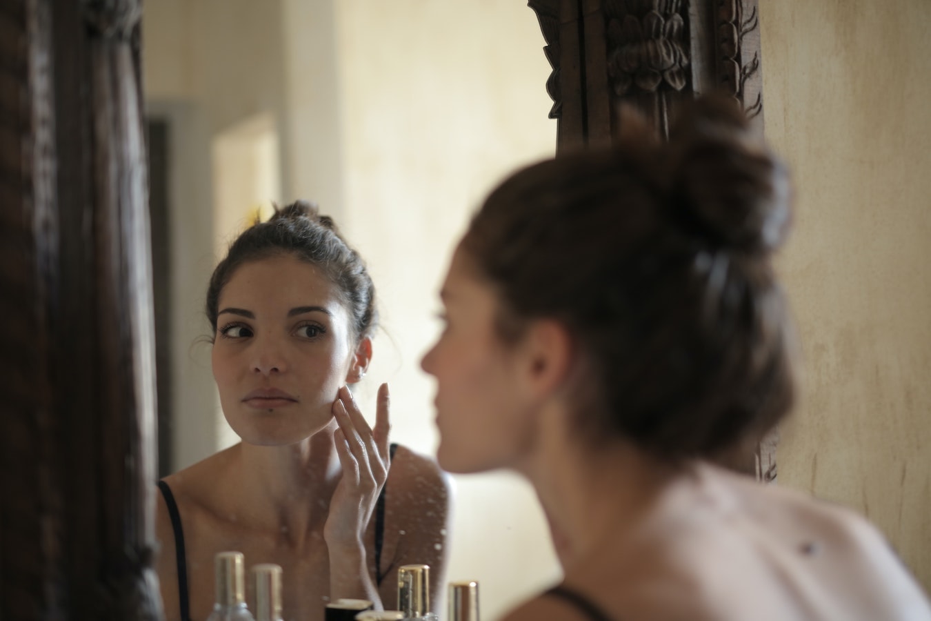 junge Frau schaut sich im Spiegel an und betreibt Hautpflege mit Nelkenöl
