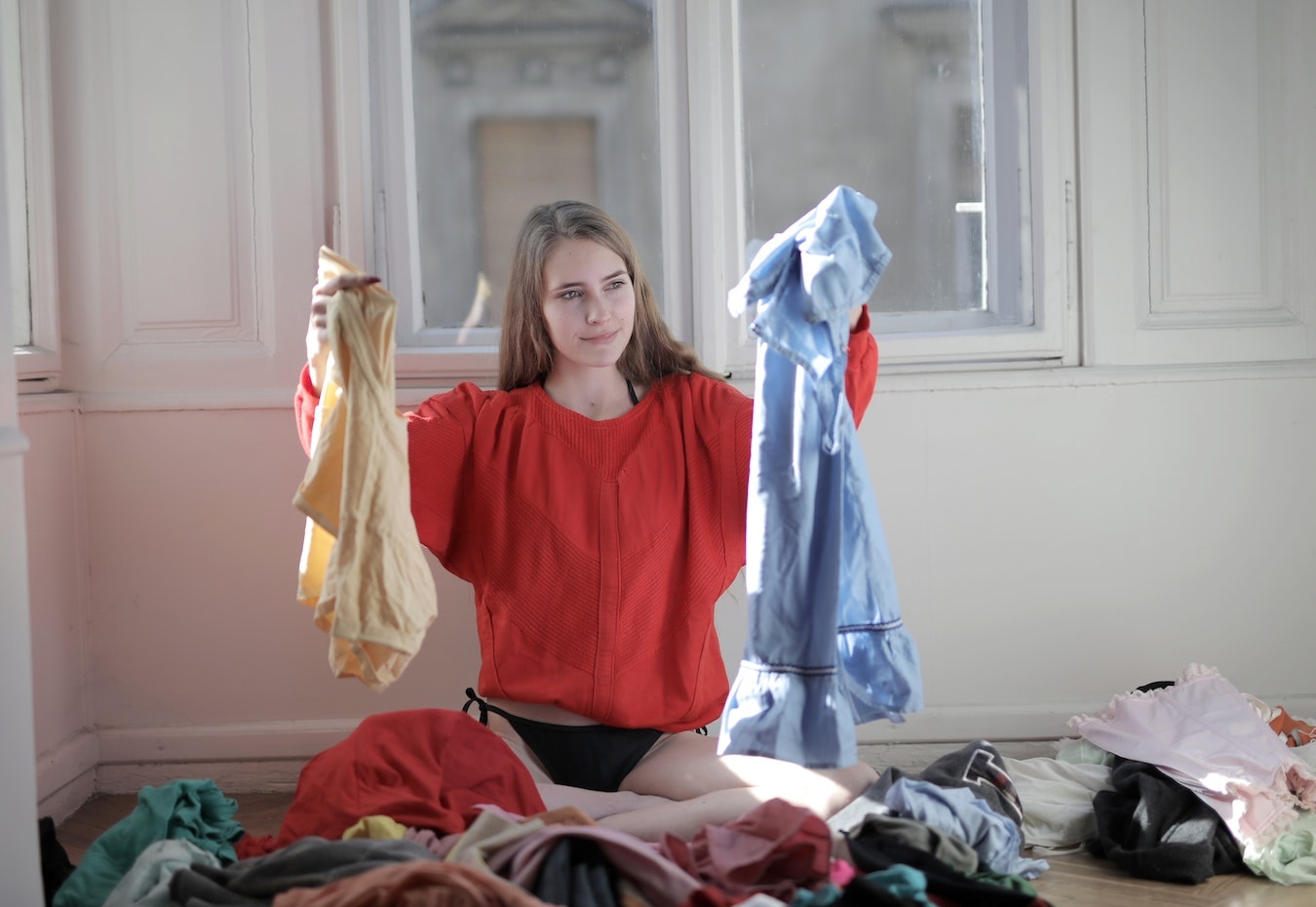 junge Frau sitzt auf ihrem Bett voller Klamotten und kann sich nicht entscheiden was sie anziehen soll