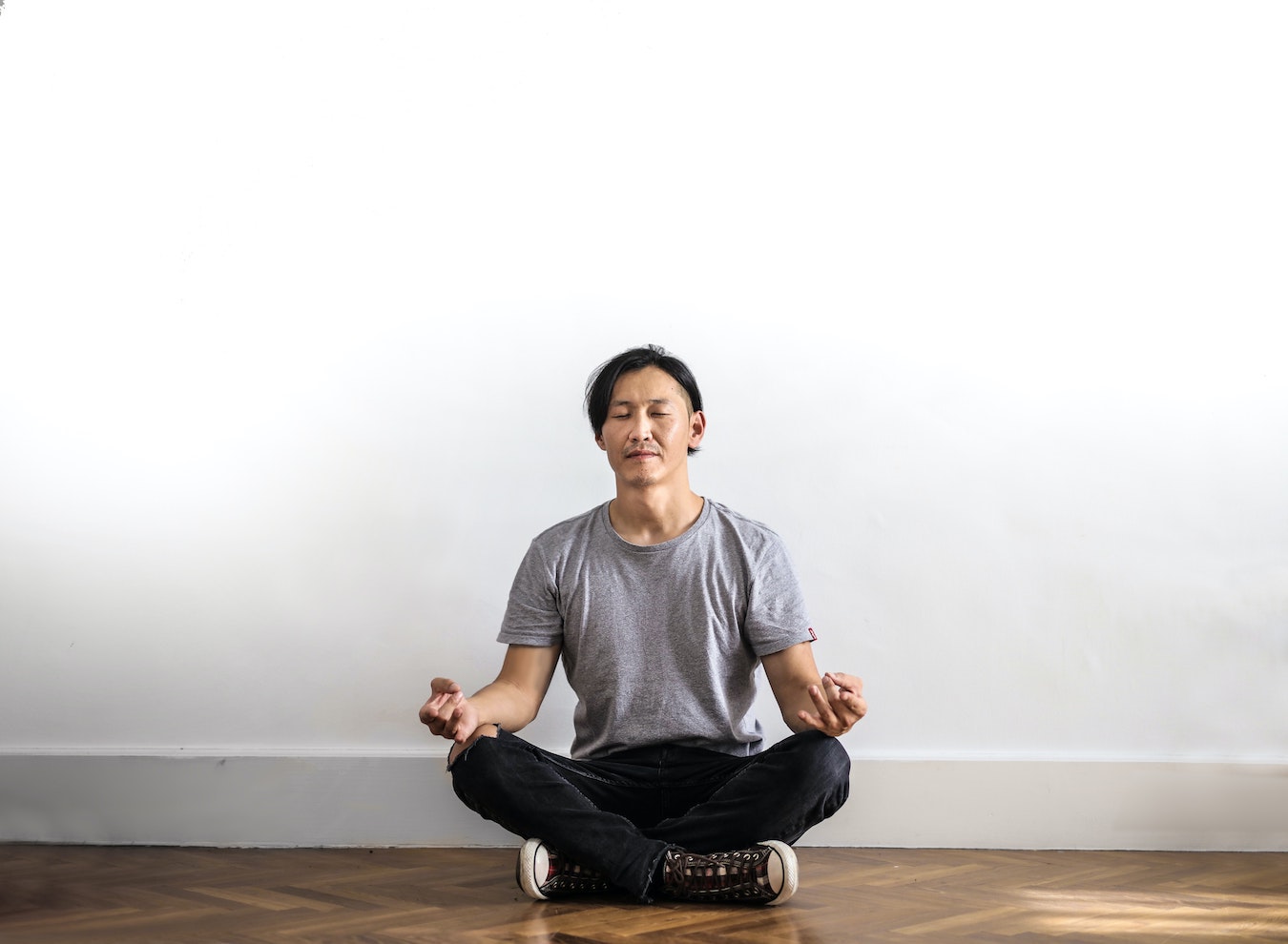 junger Mann meditiert vor einer weißen Wand um seine Selbstzweifel zu überwinden