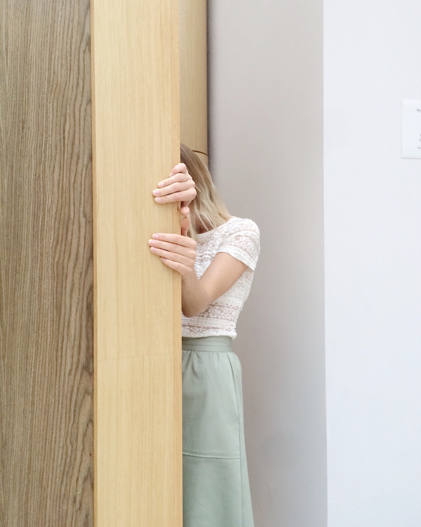 junge Frau versteckt sich hinter einer Tür aus Angst vor Ablehnung