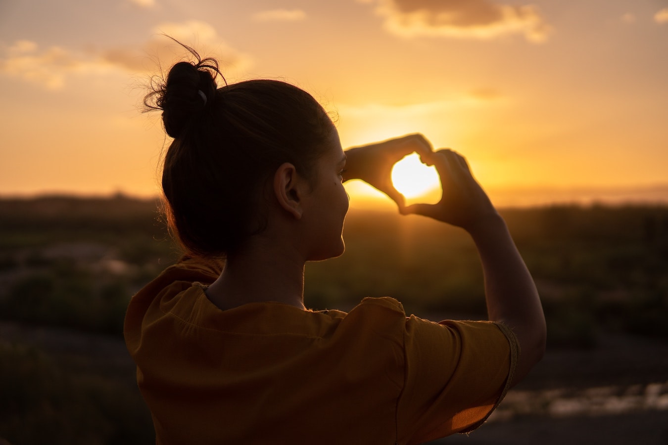 junge Frau hält ihre Hände in Herzform selbstbewusst vor die Sonne
