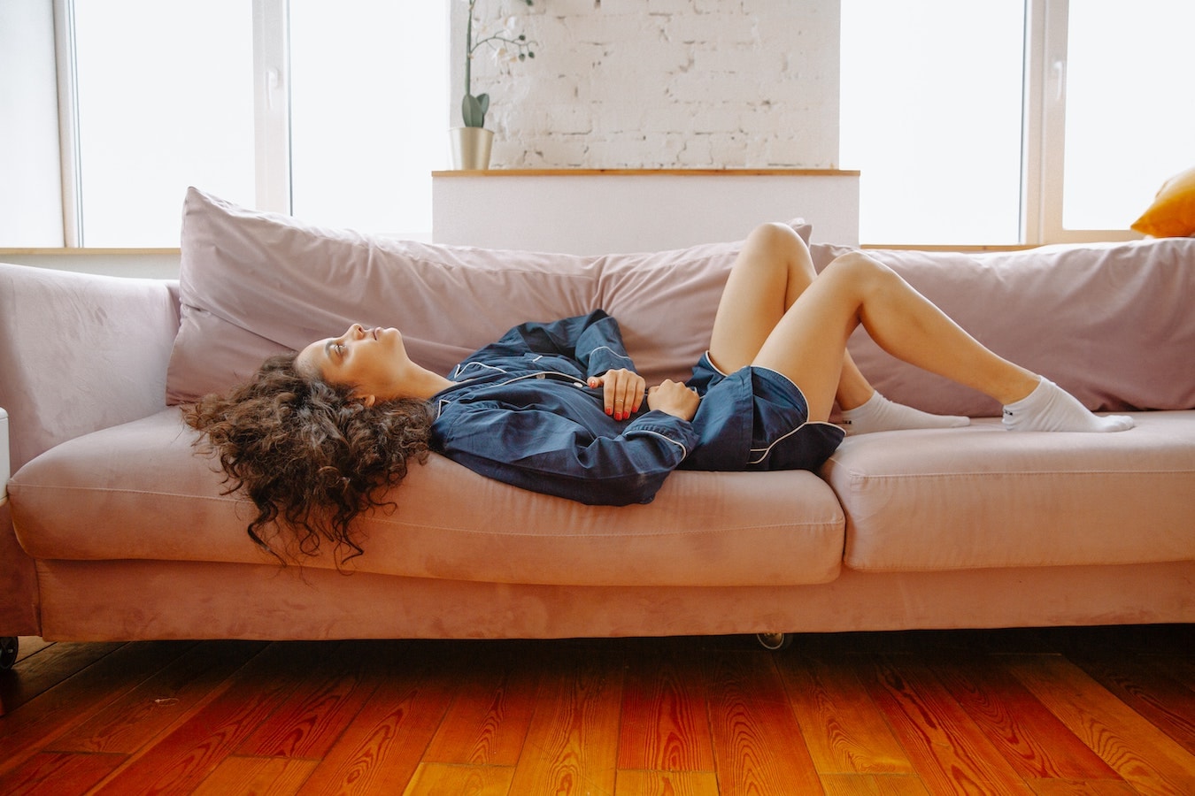 junge Frau liegt auf der Couch und hat Bauchschmerzen - Nelkenöl hilft gegen Magenschmerzen