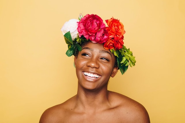 junge Frau mit Blumenkranz auf dem Kopf lächelt und strahlt voller Selbstliebe und Selbstbewusstsein