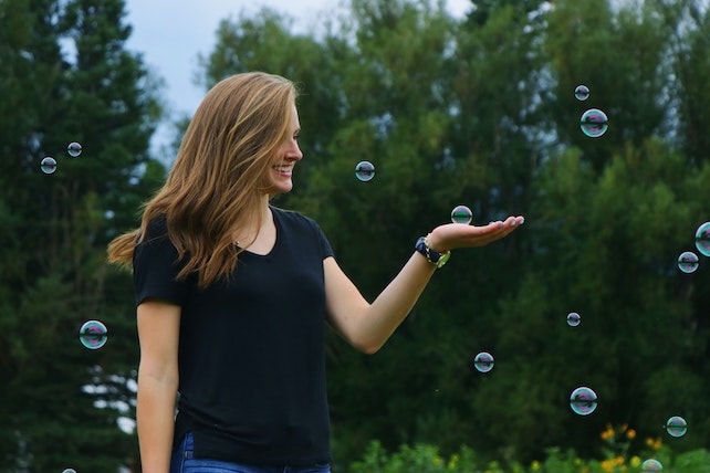 Junge Frau mit positiven Gedanken spielt mit Seifenblasen und ist glücklich