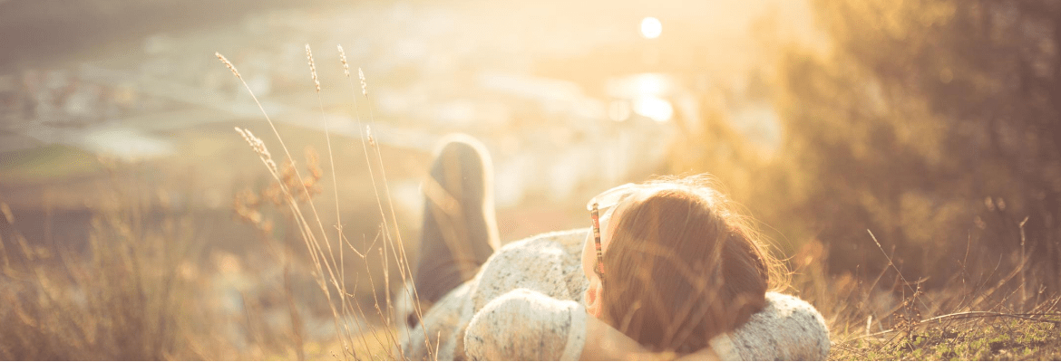 junge Person liegt entspannt und sorgenfrei im Gras und schaut in die Sonne