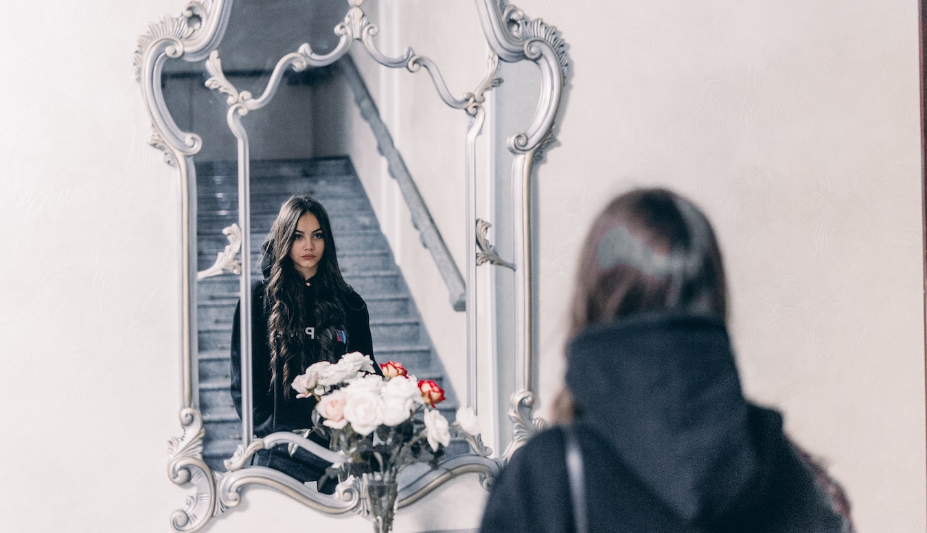 junge Frau schaut in den Spiegel leidet an Selbstsabotage und Manipulation