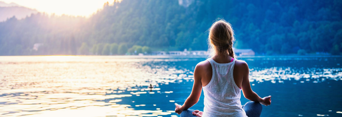 junge Frau sitzt am See und meditiert um sich mit ihrem höheren selbst zu verbinden