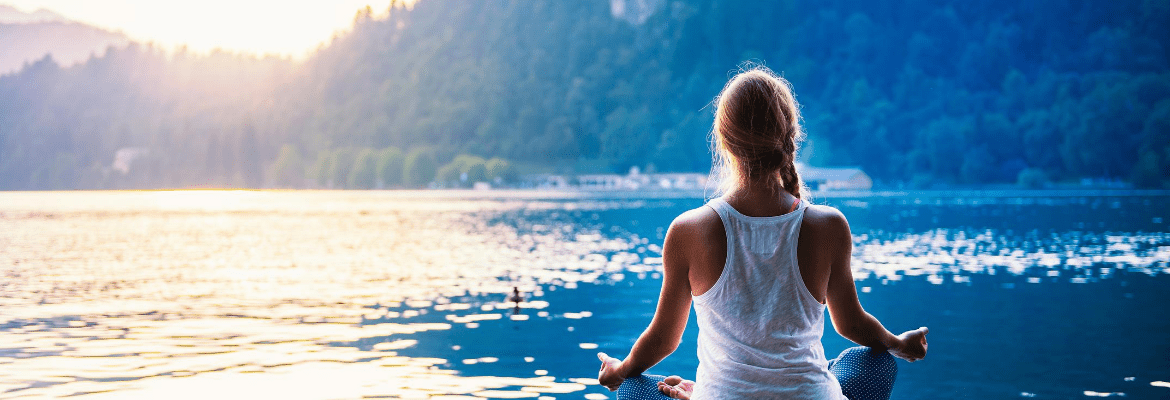 junge Frau sitzt am See und meditiert um sich mit ihrem höheren selbst zu verbinden