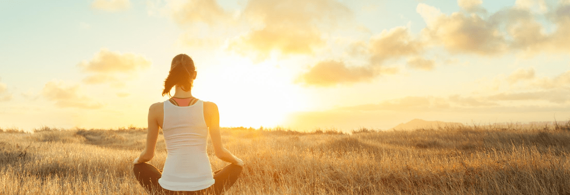 junge Frau meditiert auf einem Feld beim Sonnenuntergang um negative Gedanken loszuwerden
