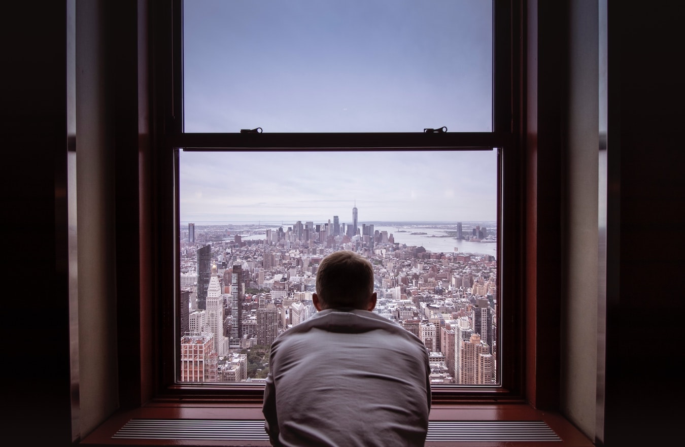 junger Mann schaut aus dem Fenster um seine negativen Gedanken loszuwerden