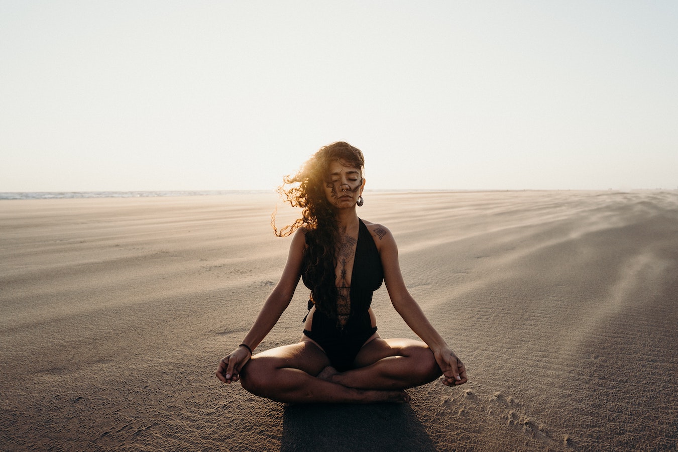 junge Frau im schwarzen Badeanzug sitzt alleine in der Wüste auf dem Sand und verbindet sich mit ihrem höheren selbst durch Meditation