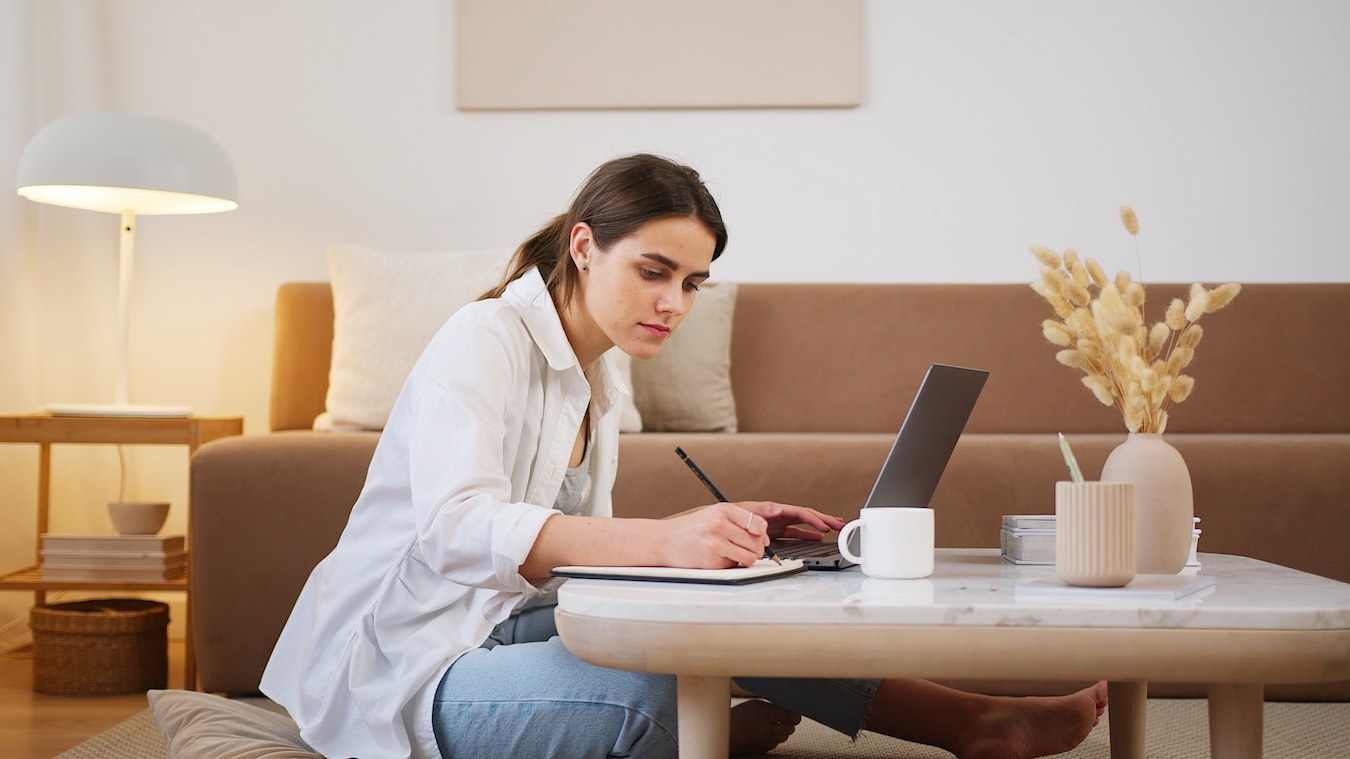 junge Frau sitzt am Schreibtisch mit ihrem Laptop und macht Notizen für ihre Hypnose Ausbildung Coaching