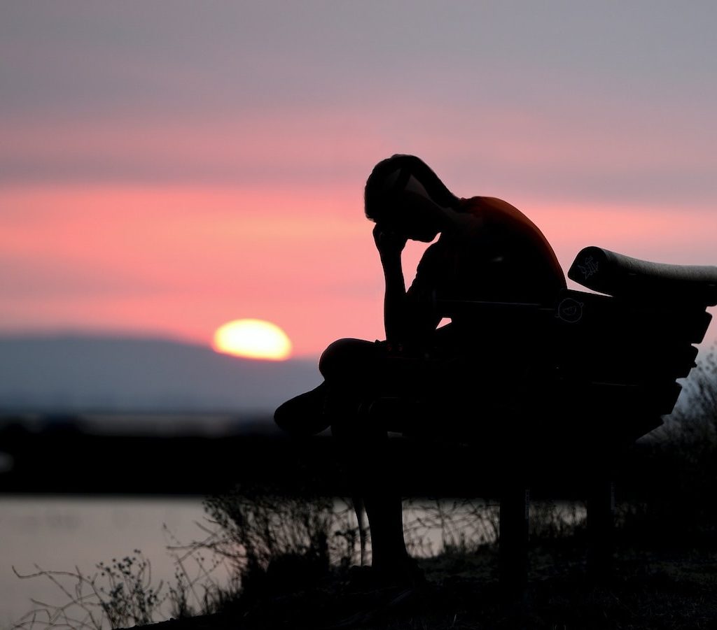 junger Mann sitzt mit gesunkenem Kopf und depressive Stimmung alleine auf einer Bank und denkt nach - Ursachen für Faulheit