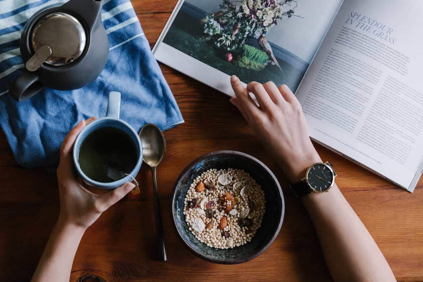 Frau trinkt Tee, isst Müsli und liest Buch als Teil ihrer Morgenroutine
