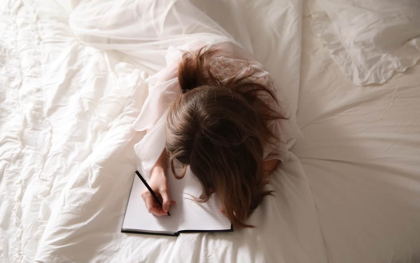 Frau schreibt Tagebuch Journal im Bett
