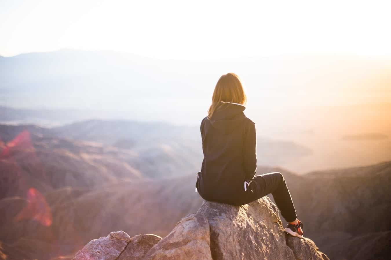 junge Frau sitzt an einem Fels und stellt sich etwas vor