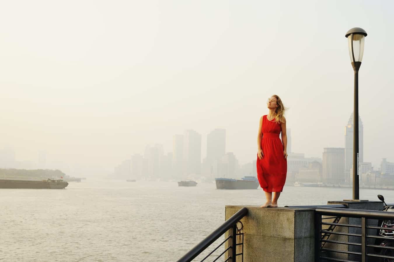 Frau in rotem Kleid steht am Wasser und hat einen guten Start in den Tag