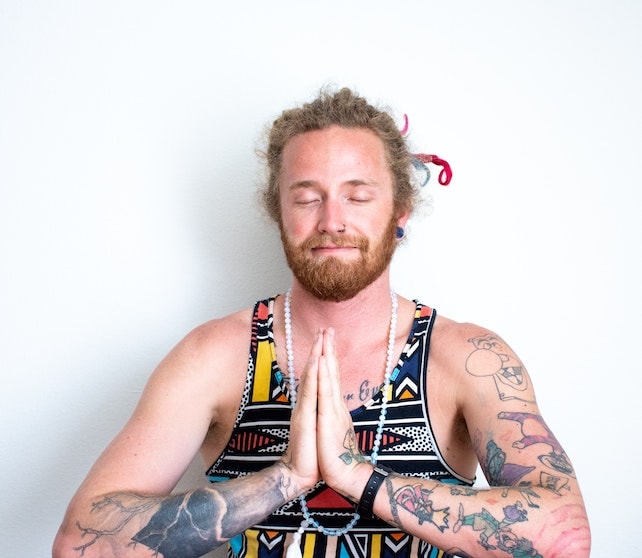 Meditation junger Mann mit langen Haaren hält seine Hände vor der Brust zusammen und meditiert für mehr Selbstliebe