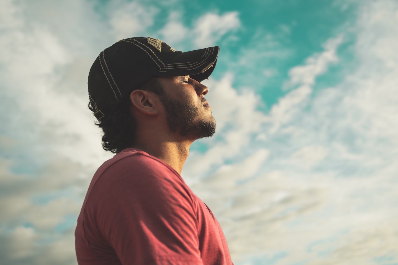 junger Mann mit Cap schaut nachdenklich in den Himmel und will seine negativen Gedanken loswerden