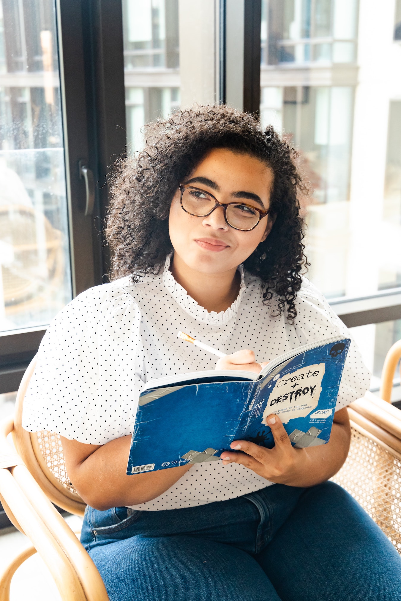 junge Frau sitzt auf einem Stuhl und hält ein Buch, in dem sie ihre negativen Denkmuster aufschreibt