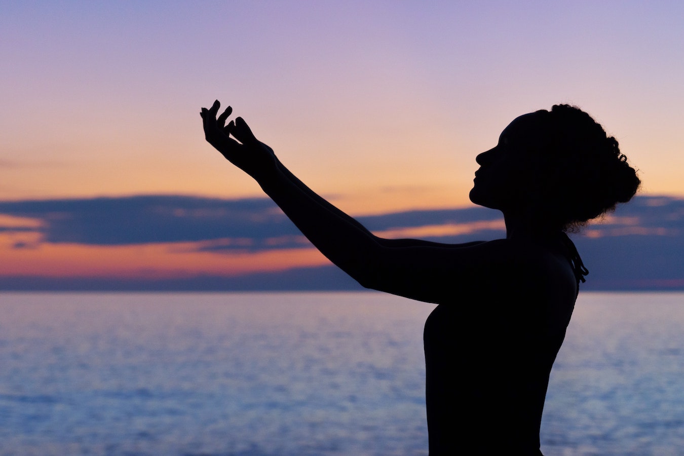 Schatten einer jungen Frau vor dem Sonnenuntergang, die ihre Arme ausstreckt - Energie, Heilung