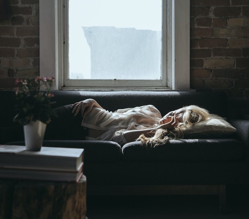 junge blonde Frau ist faul, müde und träge. Sie legt auf der Couch und hat Schwierigkeiten ihre Faulheit zu überwinden
