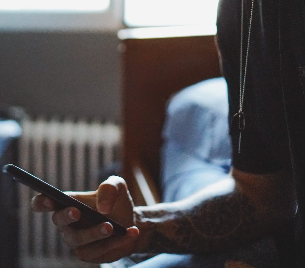 tätowierte Hand hält ein Smartphone - Ablenkung vermeiden und Faulheit überwinden