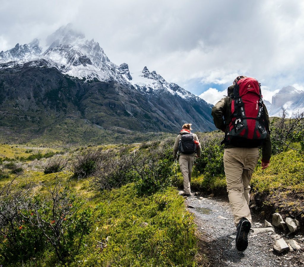zwei junge Leute mit Rucksäcken wandern in den Bergen - Bewegung gegen Faulheit